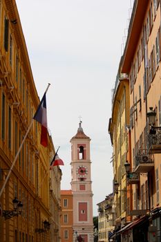Beautiful view of a narrow street leading to a historic clock tower in a quaint European town.