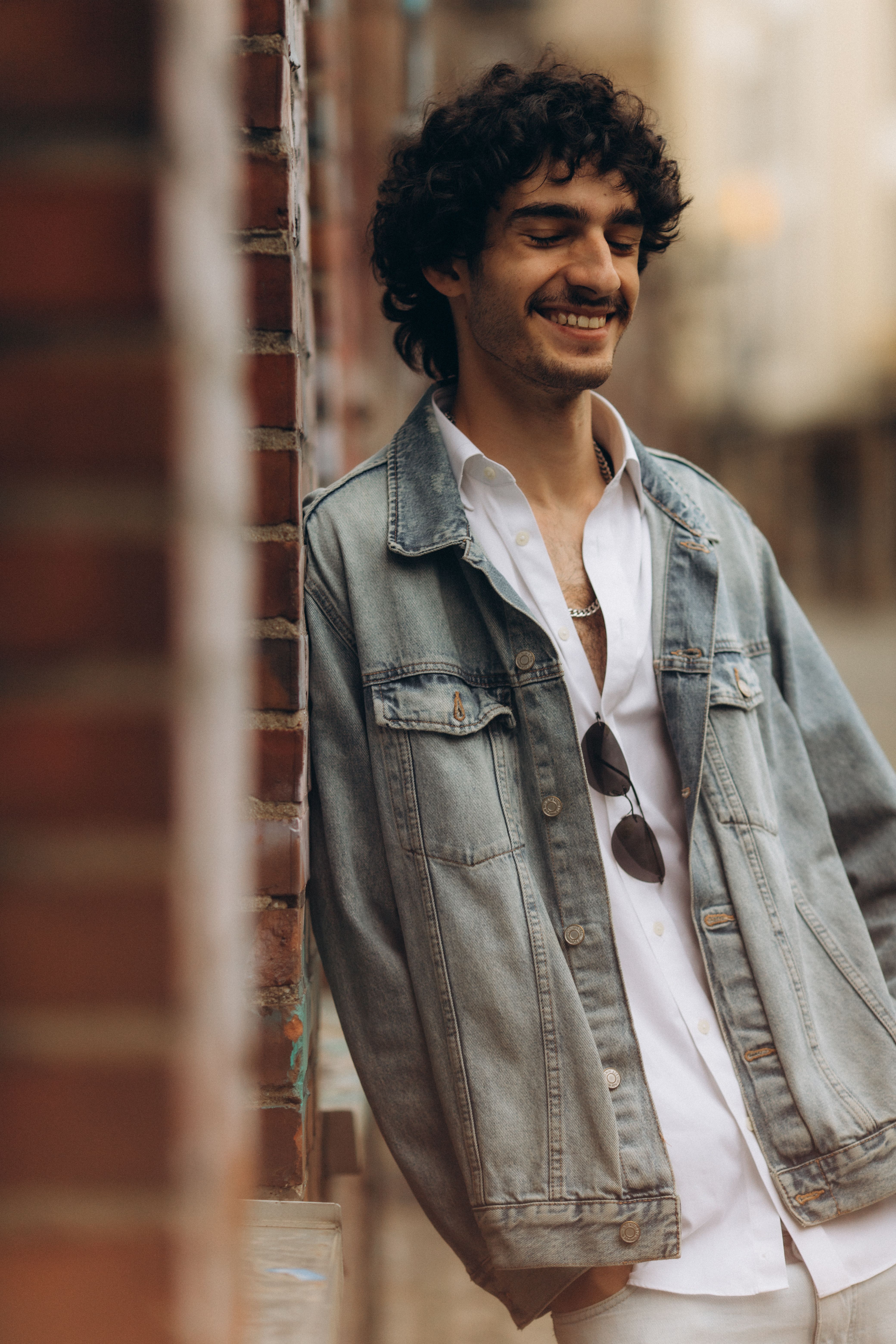 A man in a denim jacket leaning against a brick wall · Free Stock Photo