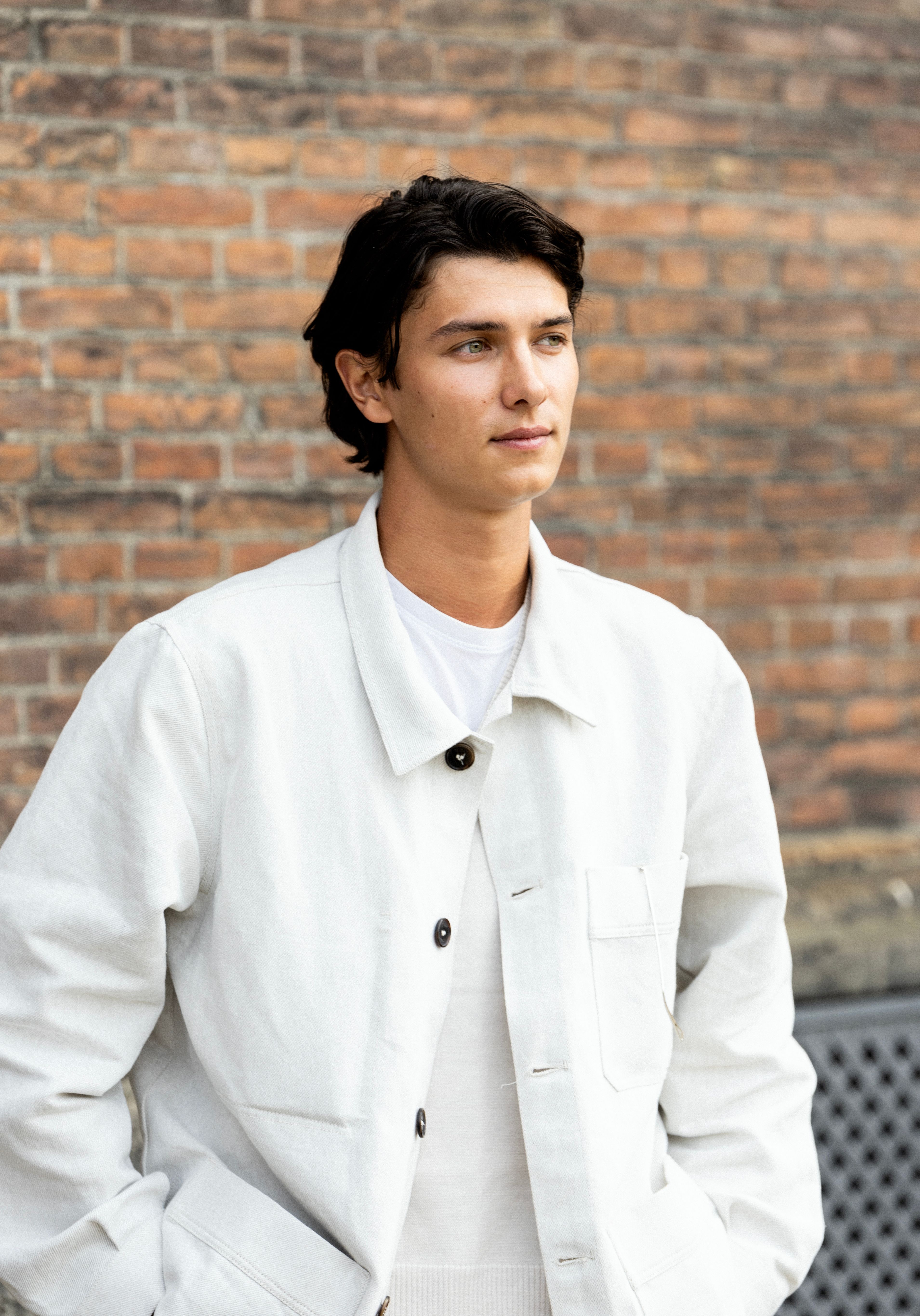Stylish young man in white jacket posing against a brick wall in København, Denmark.