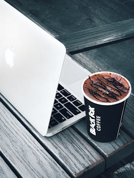 A sleek laptop and a cup of coffee on a wooden table evoke productivity in a relaxed outdoor setting.