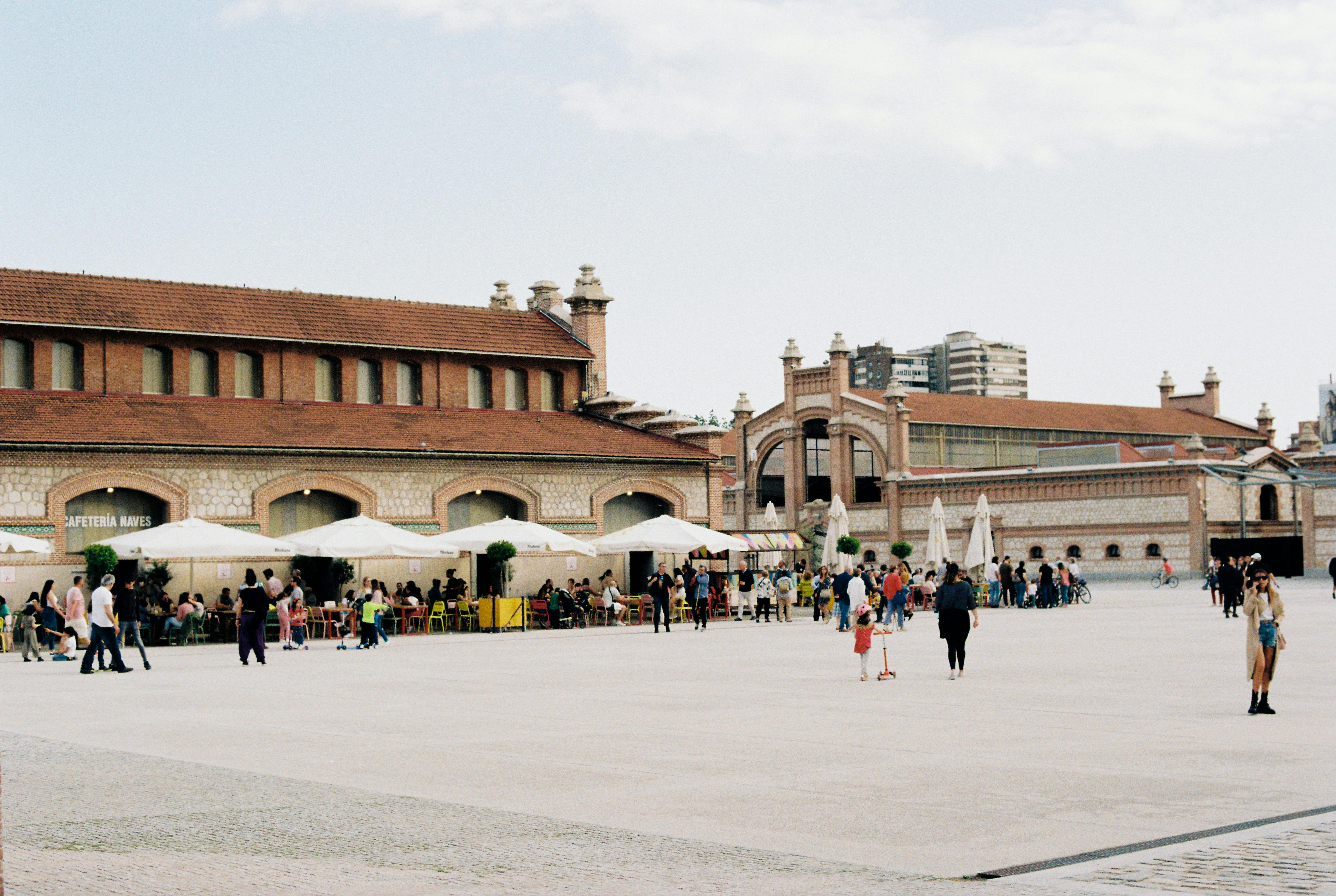 A lively scene at a public plaza with people enjoying a sunny day near a historic building.