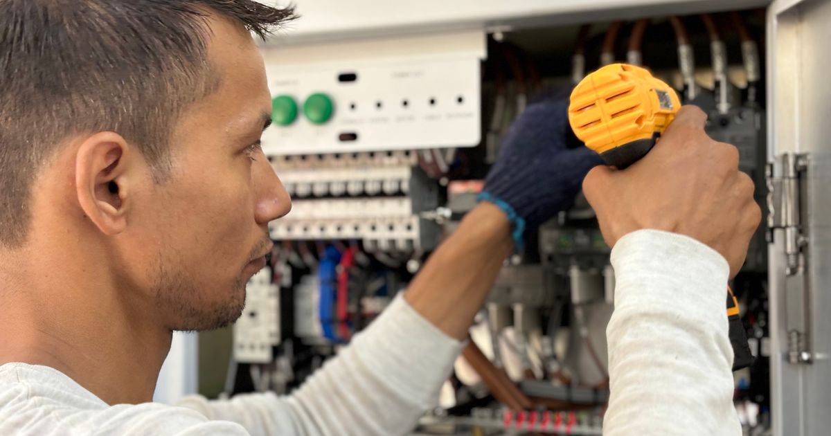 An electrician using a cordless screwdriver on a breaker panel