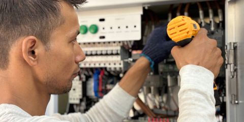 An electrician using a cordless screwdriver on a breaker panel
