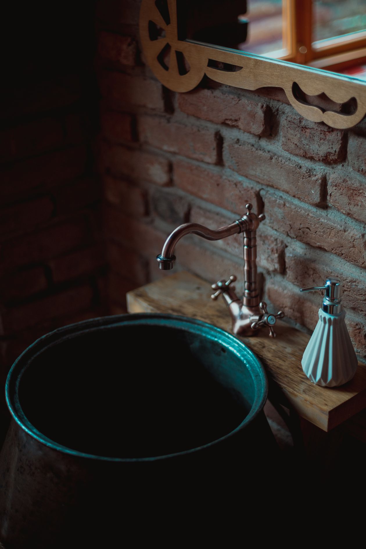 Vintage-style faucet with a dark round basin against a brick wall