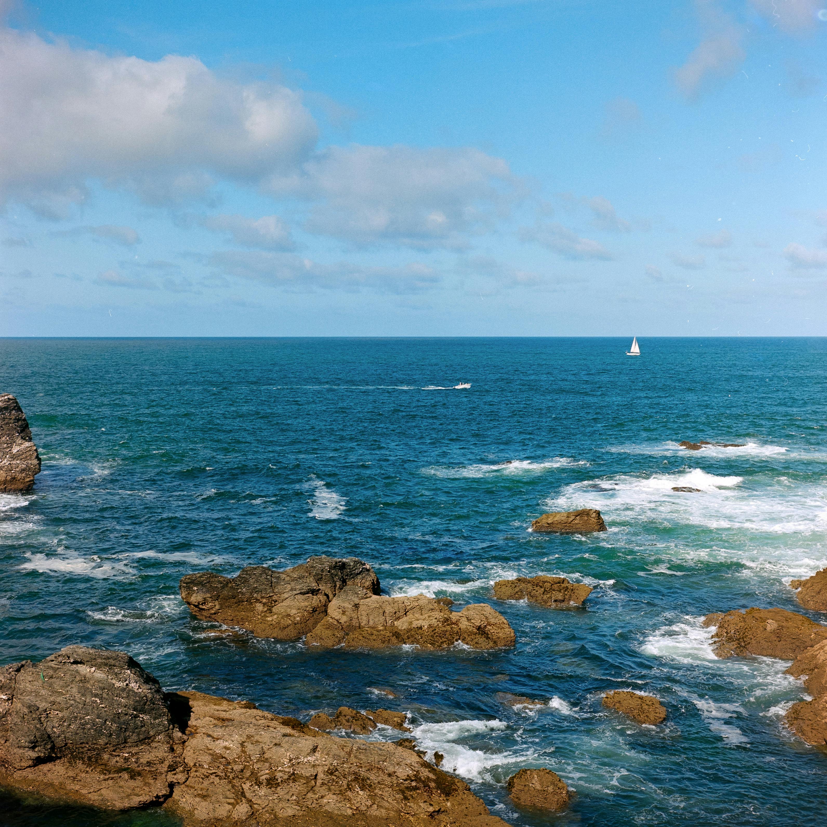 a view of the ocean with rocks and a sailboat