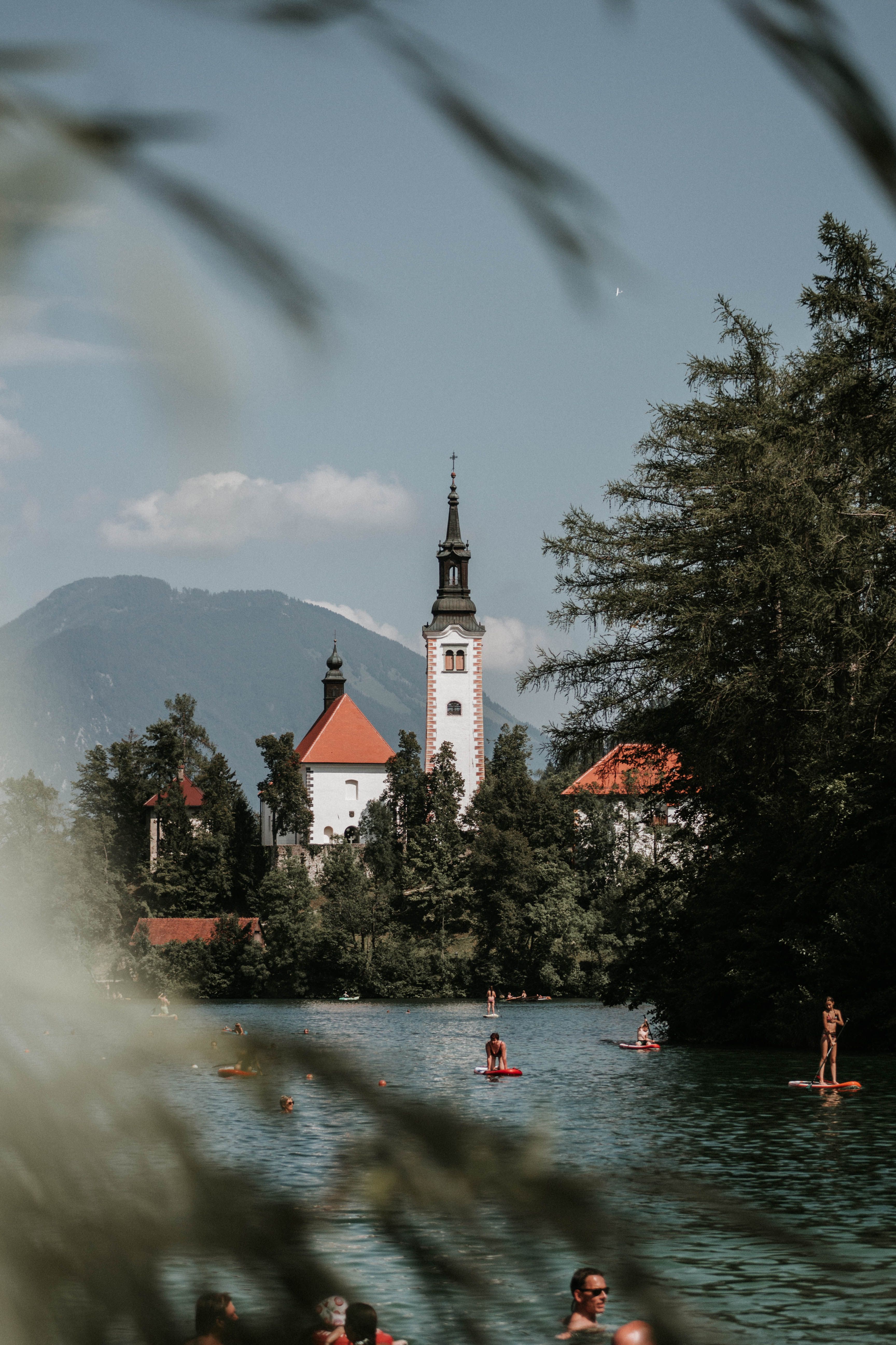 Serene Lake Bled scene with people paddleboarding and the iconic Church of Assumption in Slovenia.