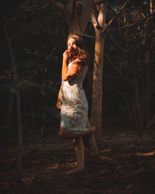 Free A young woman in a floral dress posing elegantly in a sunlit forest. Stock Photo