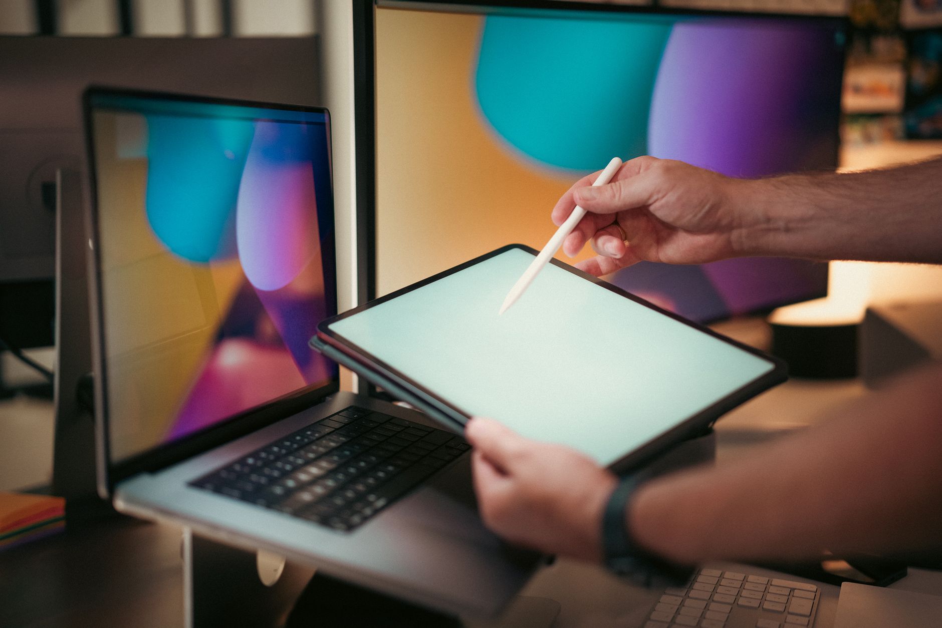 Designer using a digital pen on a tablet with colorful screens in a modern home office setting.