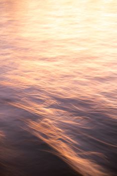 Abstract ocean waves illuminated by a warm sunset glow, creating a dreamy, artistic effect.