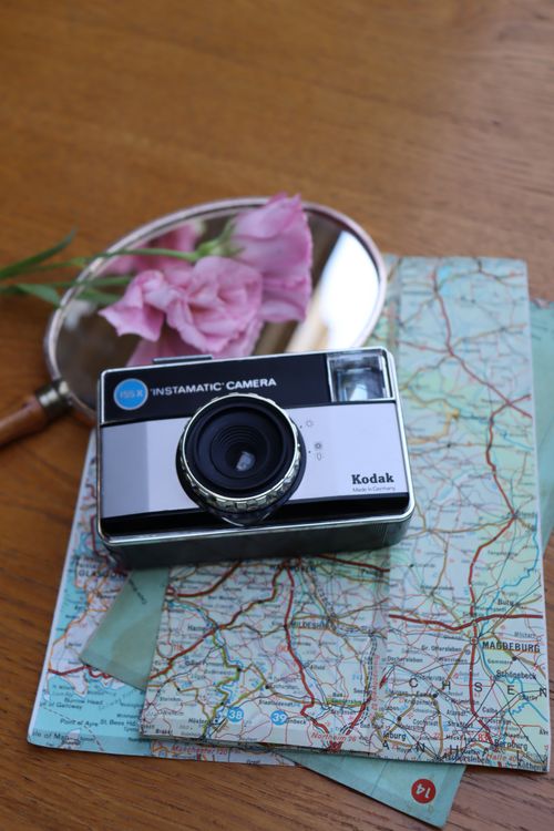 Free A vintage Kodak Instamatic camera sits on a map with pink flowers, evoking nostalgia and travel. Stock Photo