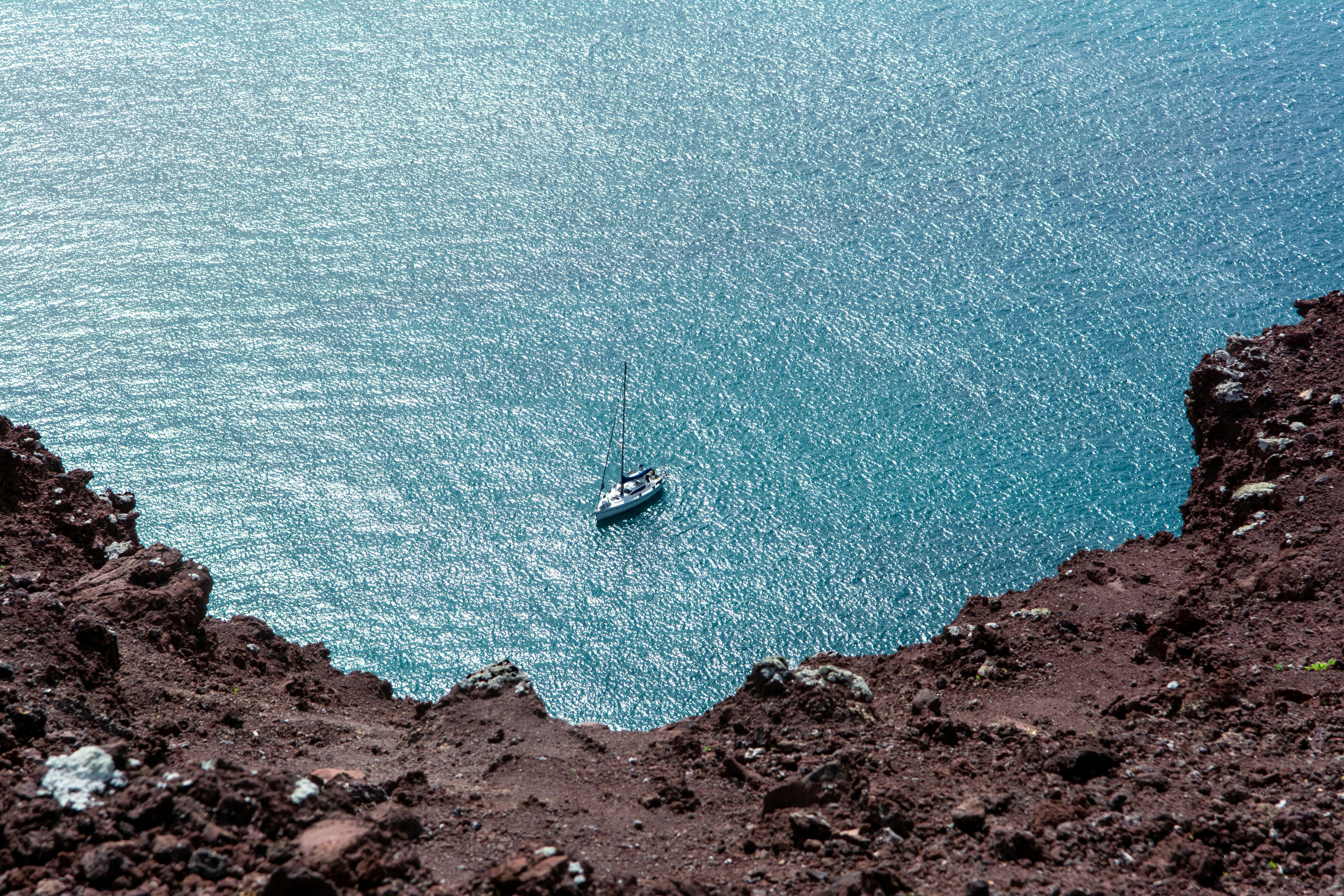 A sailboat on clear waters, seen from a rocky clifftop in Lanzarote, Spain, offers an aerial perspective.