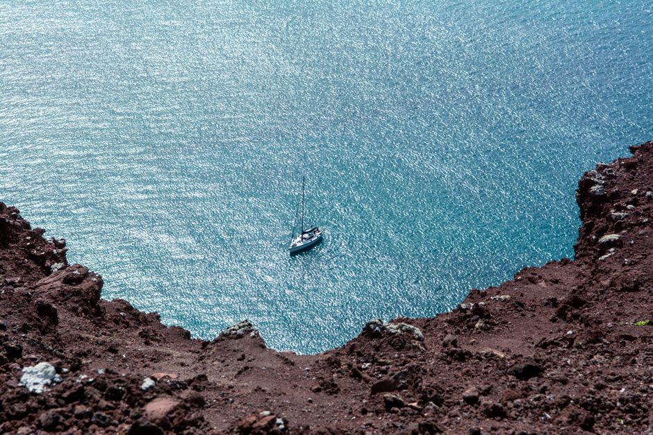 A sailboat on clear waters, seen from a rocky clifftop in Lanzarote, Spain, offers an aerial perspective.