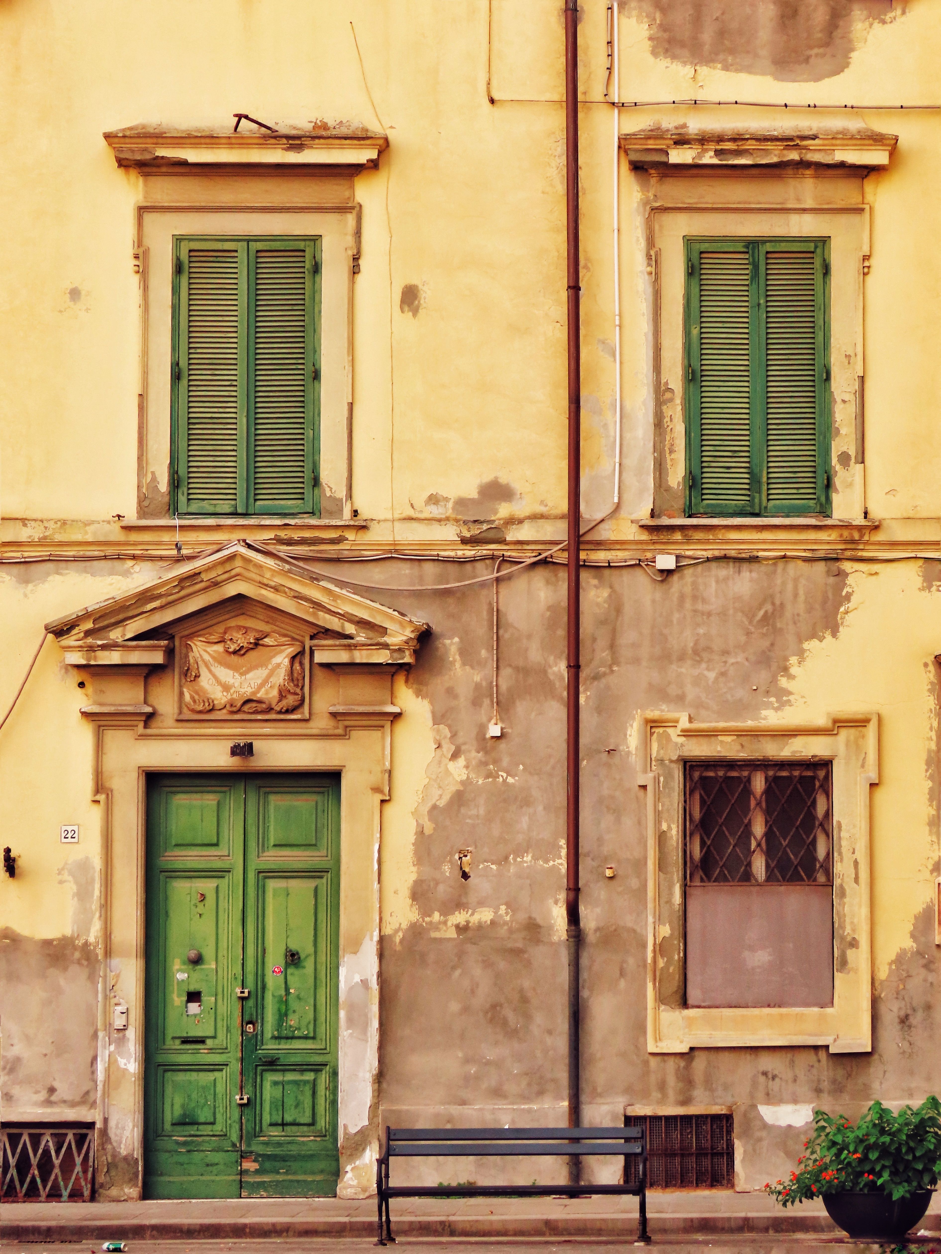 Charming aging facade of a historic building with green doors and shutters, evoking vintage European architecture.