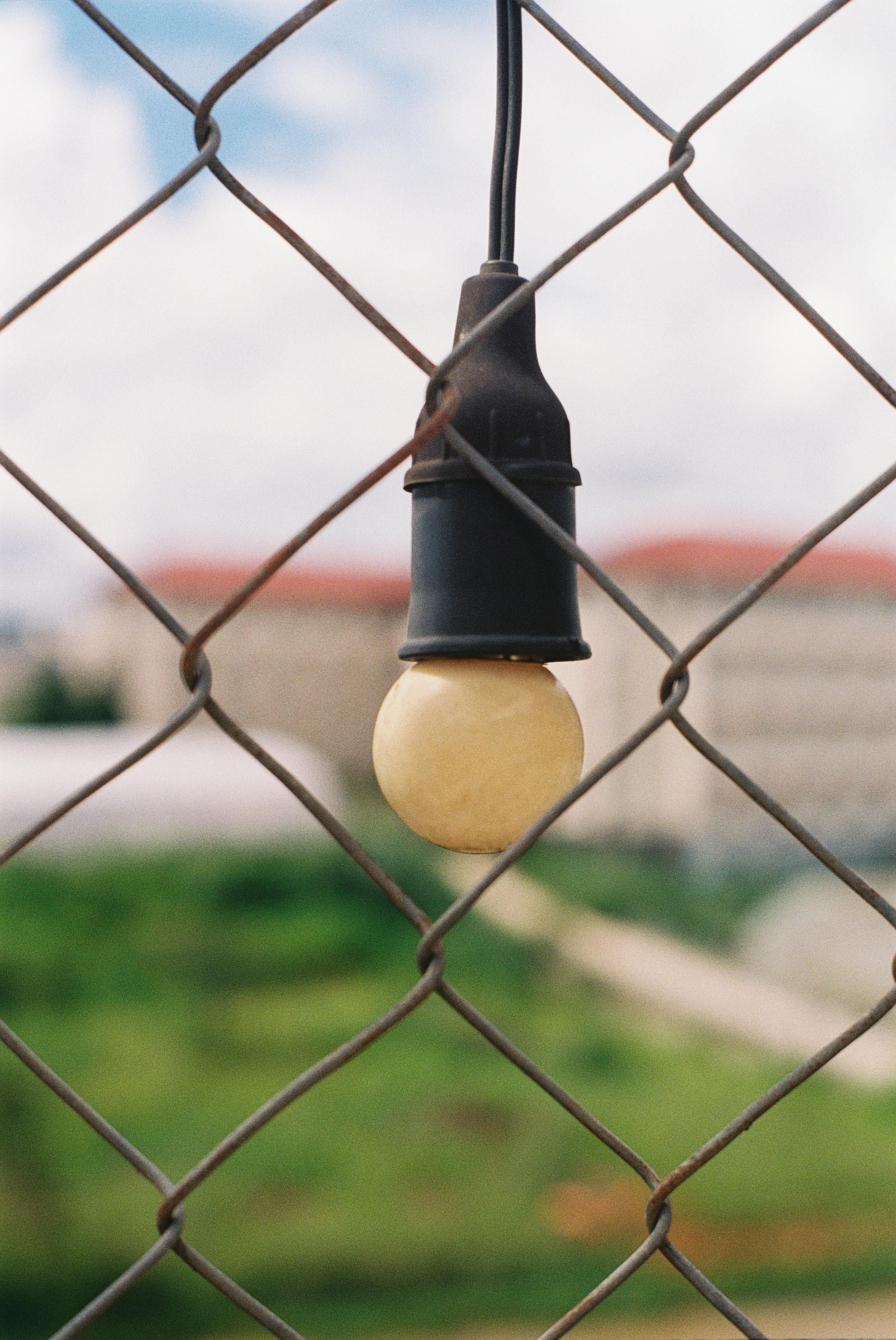 Rustic outdoor light bulb hanging from a wire against a blurred scenic background.