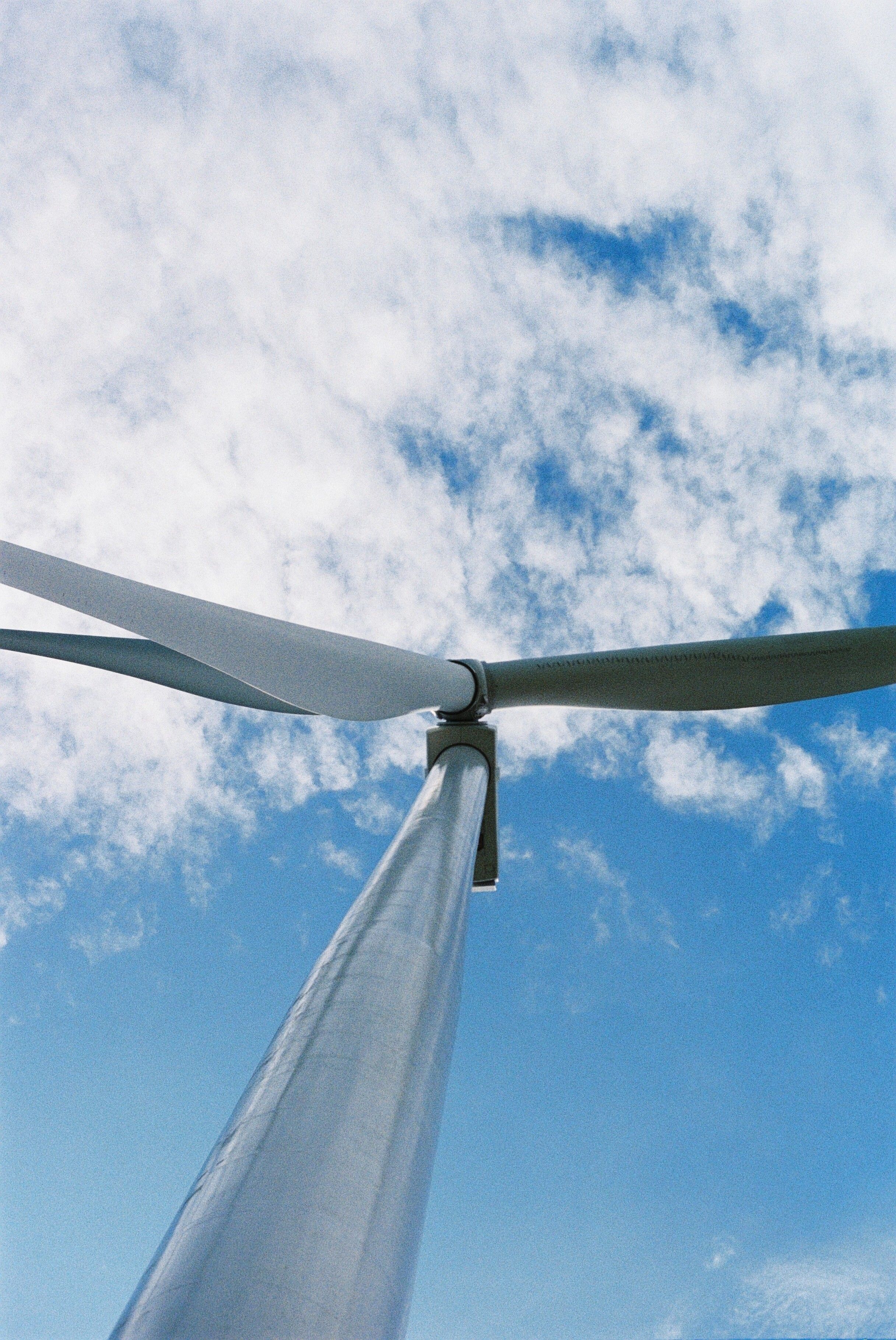 Fotomural Mirando hacia arriba a una turbina eólica con un fondo de cielo azul claro, simbolizando energía renovable.