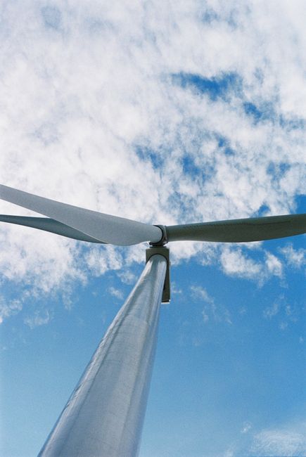 Fotomural Mirando hacia arriba a una turbina eólica con un fondo de cielo azul claro, simbolizando energía renovable.