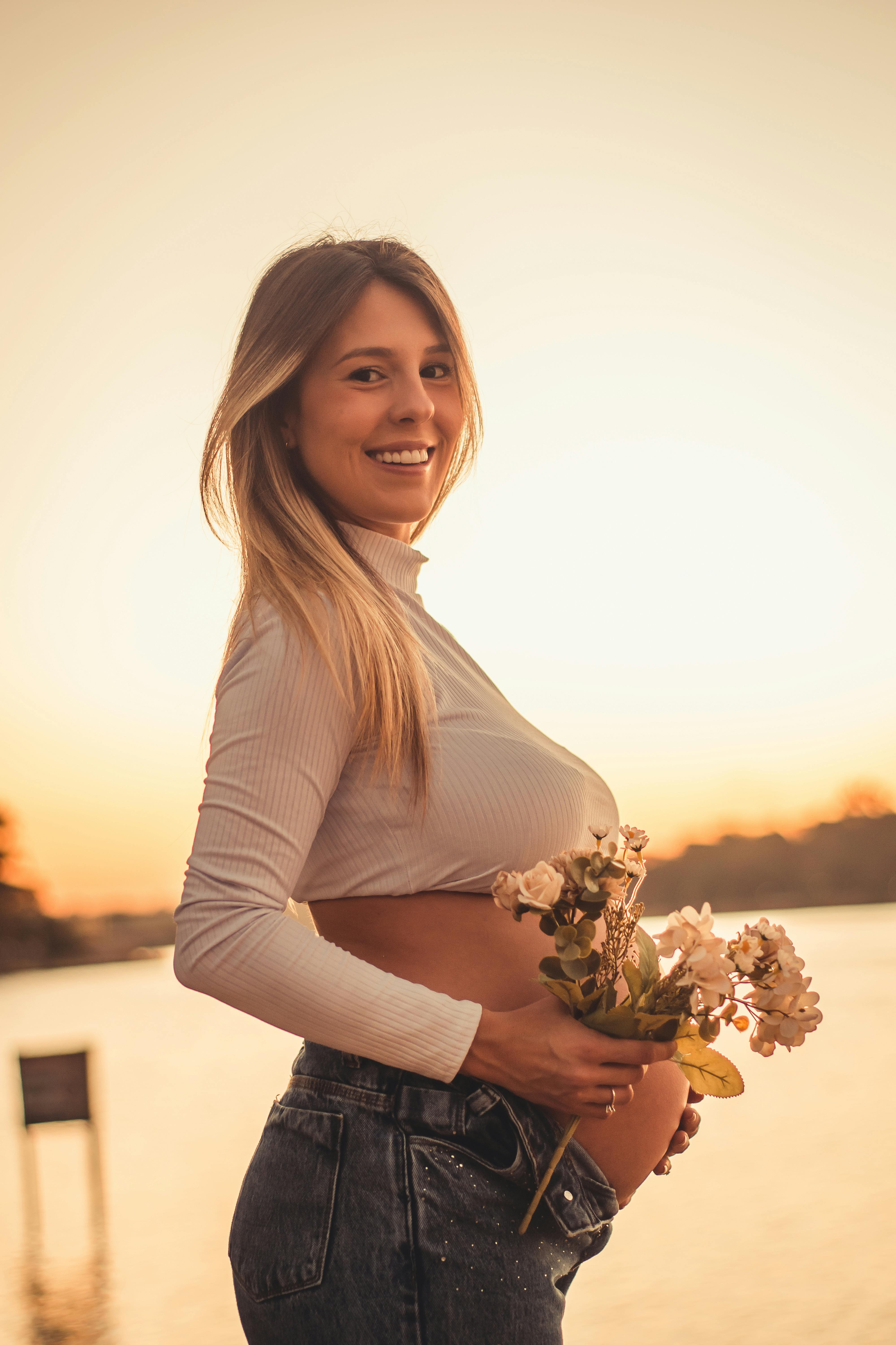 a pregnant woman holding flowers at sunset