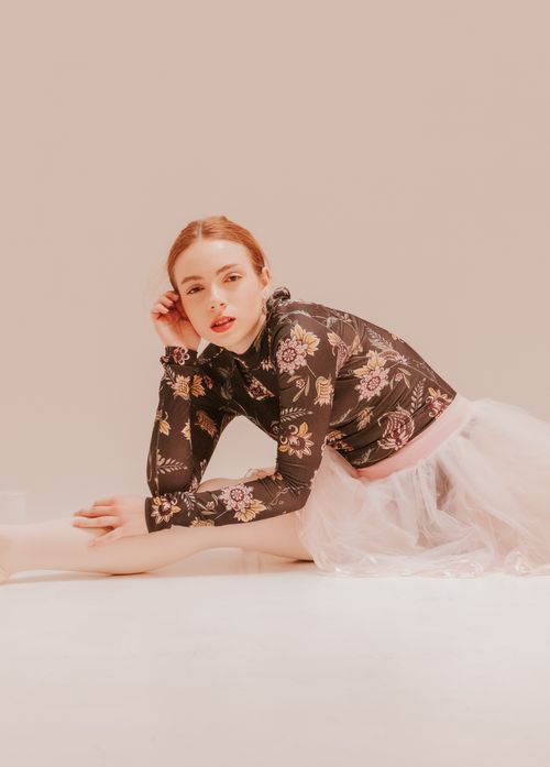 Free A young woman in a floral top and pink tulle skirt posing elegantly indoors with soft lighting. Stock Photo