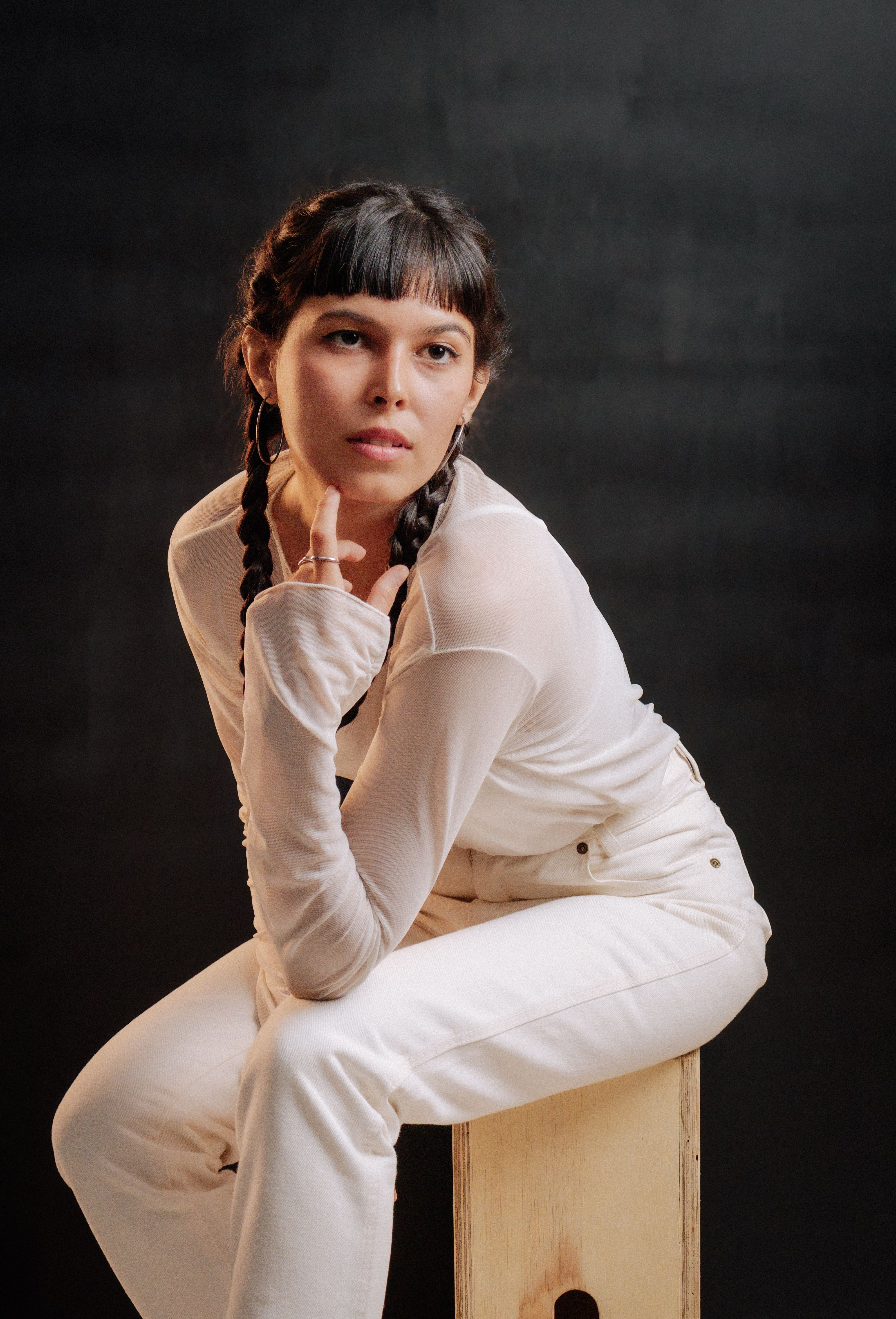 Elegant portrait of a young woman in white with braided hair, posing thoughtfully indoors.