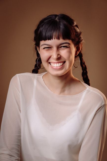 A young woman with braided hair, smiling brightly against a neutral background in São Paulo.