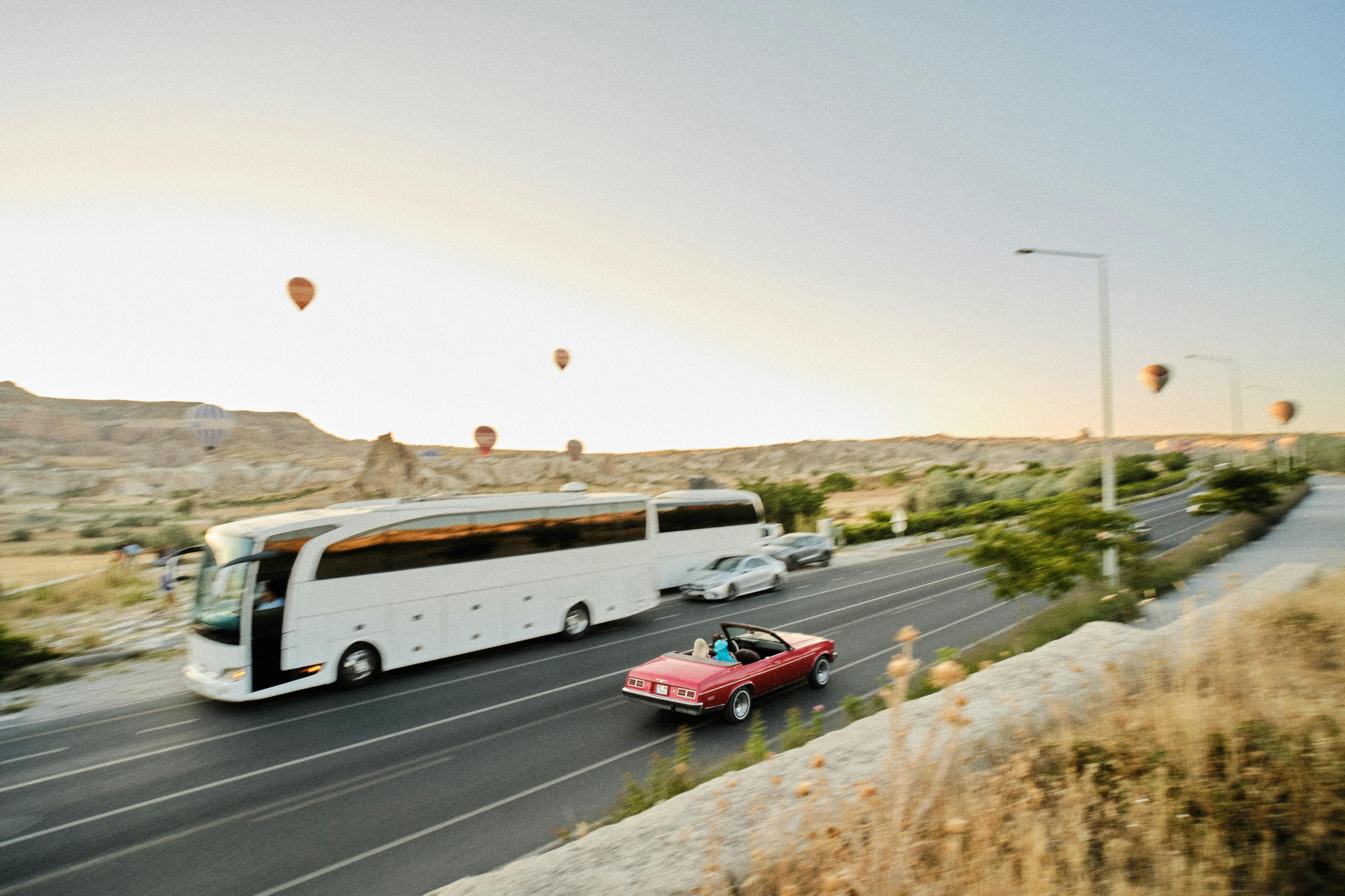 a bus driving down a road with a hot air balloon in the sky