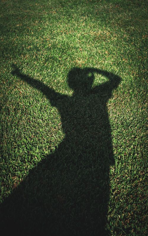 Free A person's shadow striking a dynamic pose on a vibrant green grass lawn outdoors. Stock Photo