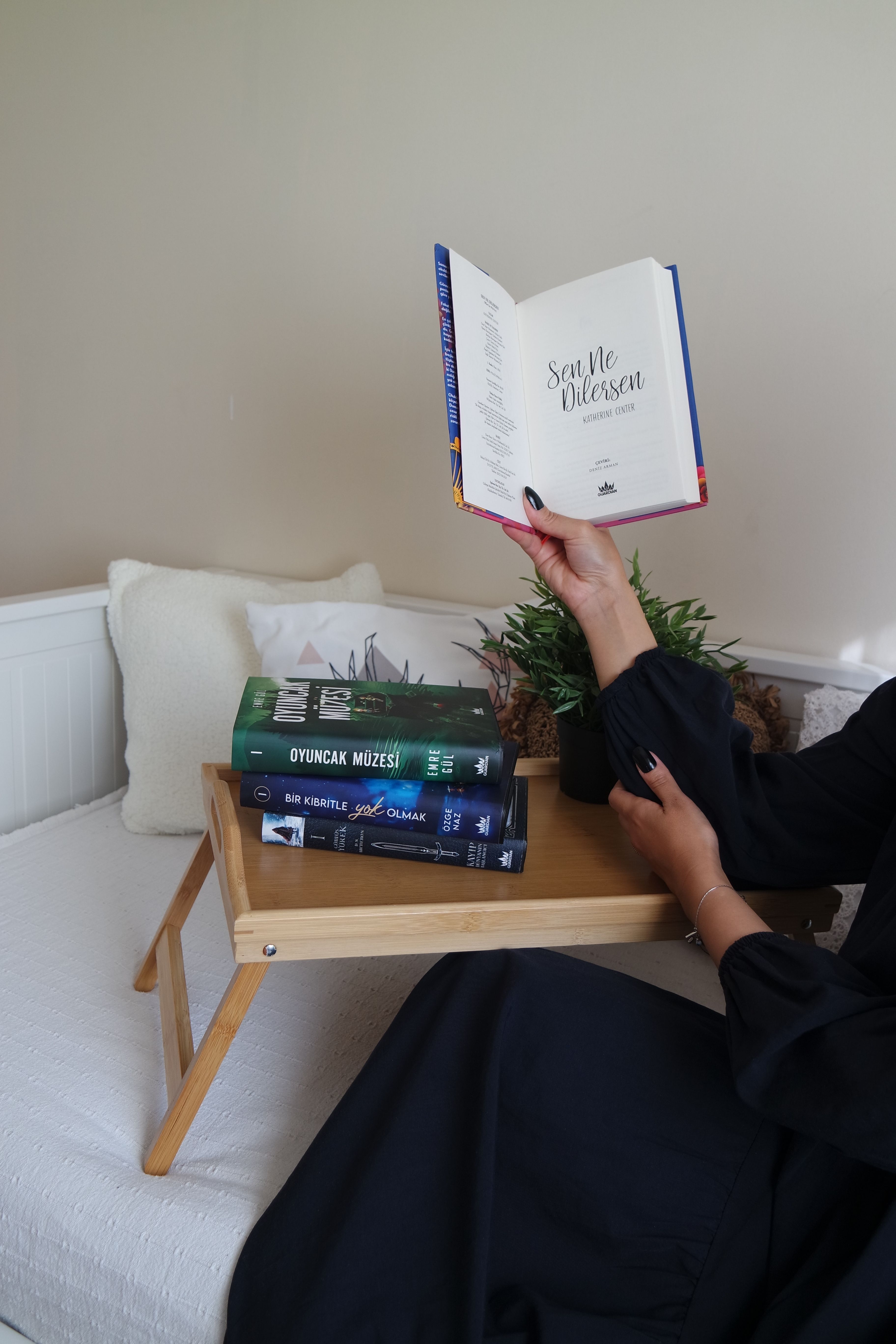 An adult reading a book with other books stacked on a wooden tray in a cozy indoor setting.