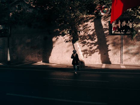A woman in shadow walking along a sunlit urban street with dramatic light and shadows.