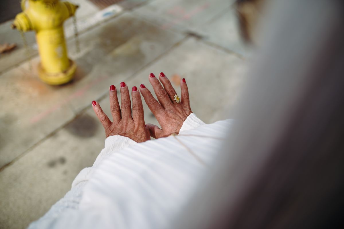 An elegant close-up of hands with red nail polish and jewelry, set against an urban outdoor backdrop.