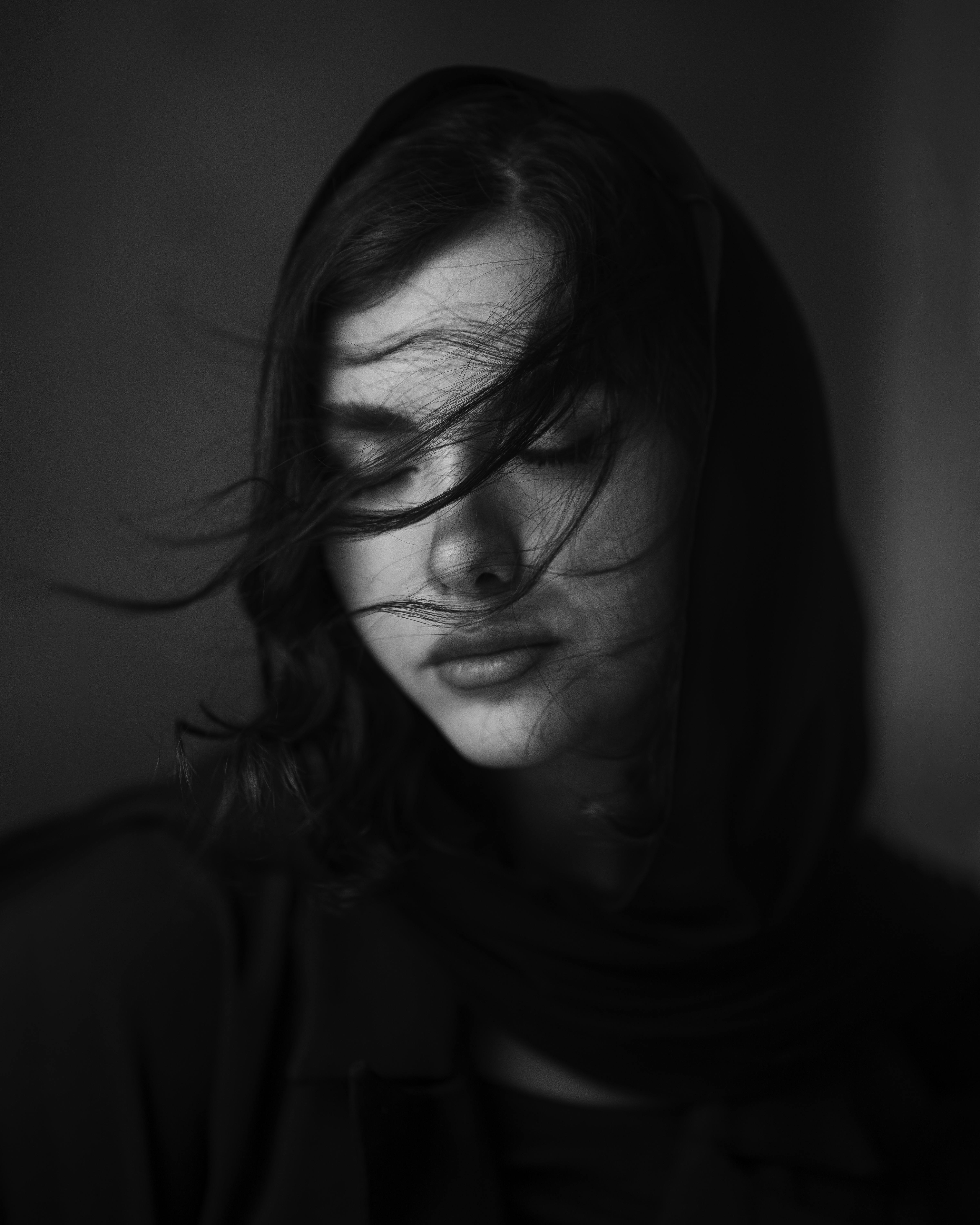 Evocative black and white portrait of a woman with wind-swept hair in a studio setting.
