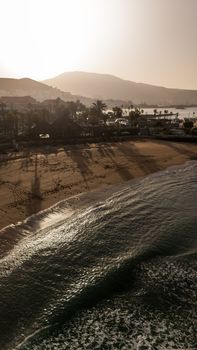 A serene beach scene at Playa de las Americas, Spain during sunset with waves and shadows.