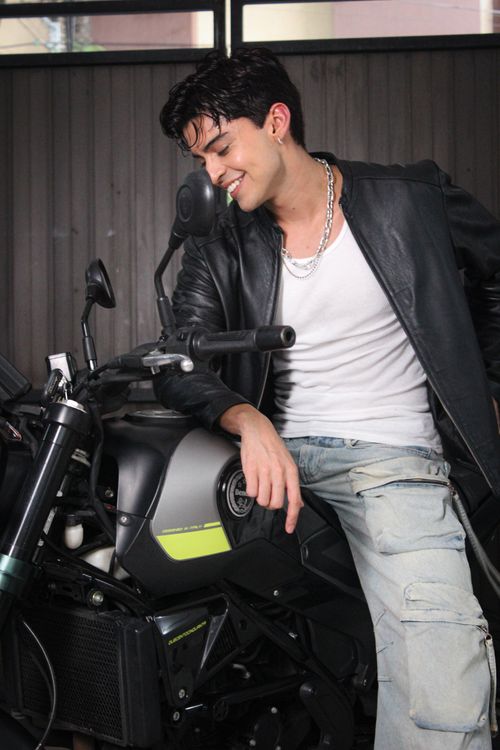 Free Confident young man in leather jacket smiling while sitting on motorcycle indoors. Stock Photo
