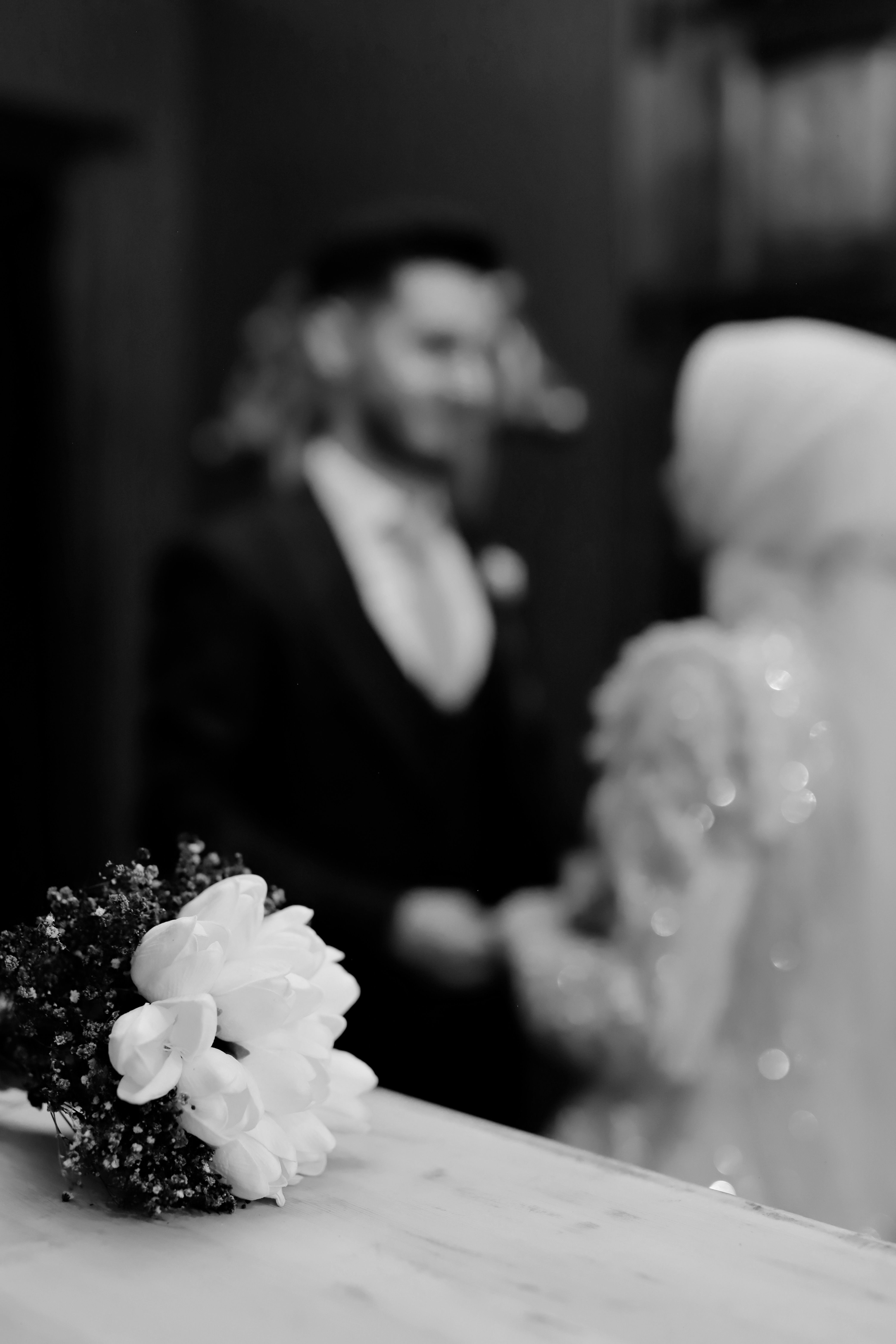 Classic black and white photo of wedding bouquet with bride and groom in soft focus.