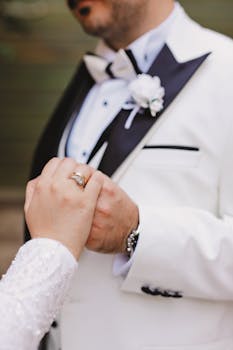 Close-up of a groom in a tuxedo holding hands with a bride, symbolizing love and commitment.