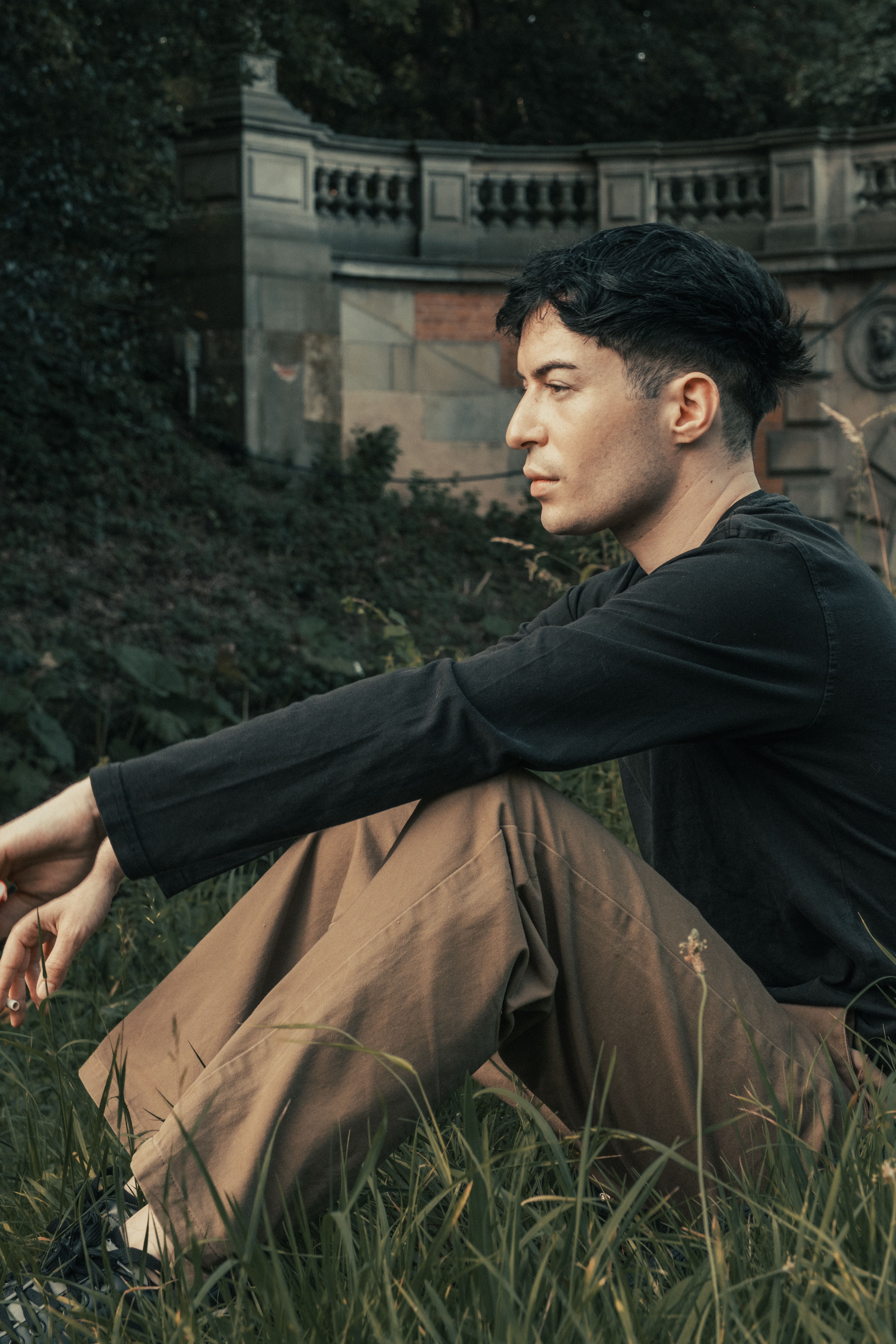 Young man sitting in an urban park, wearing a stylish outfit. Captured in a contemplative moment.