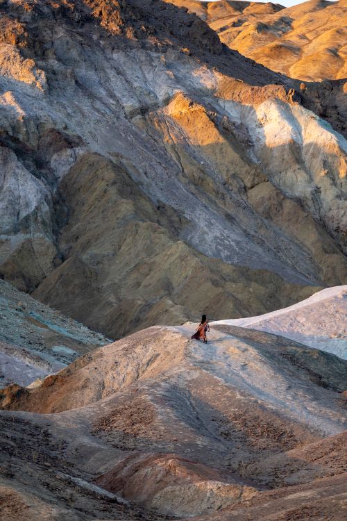 Free A lone woman explores a vibrant rocky desert landscape, casting deep shadows. Stock Photo