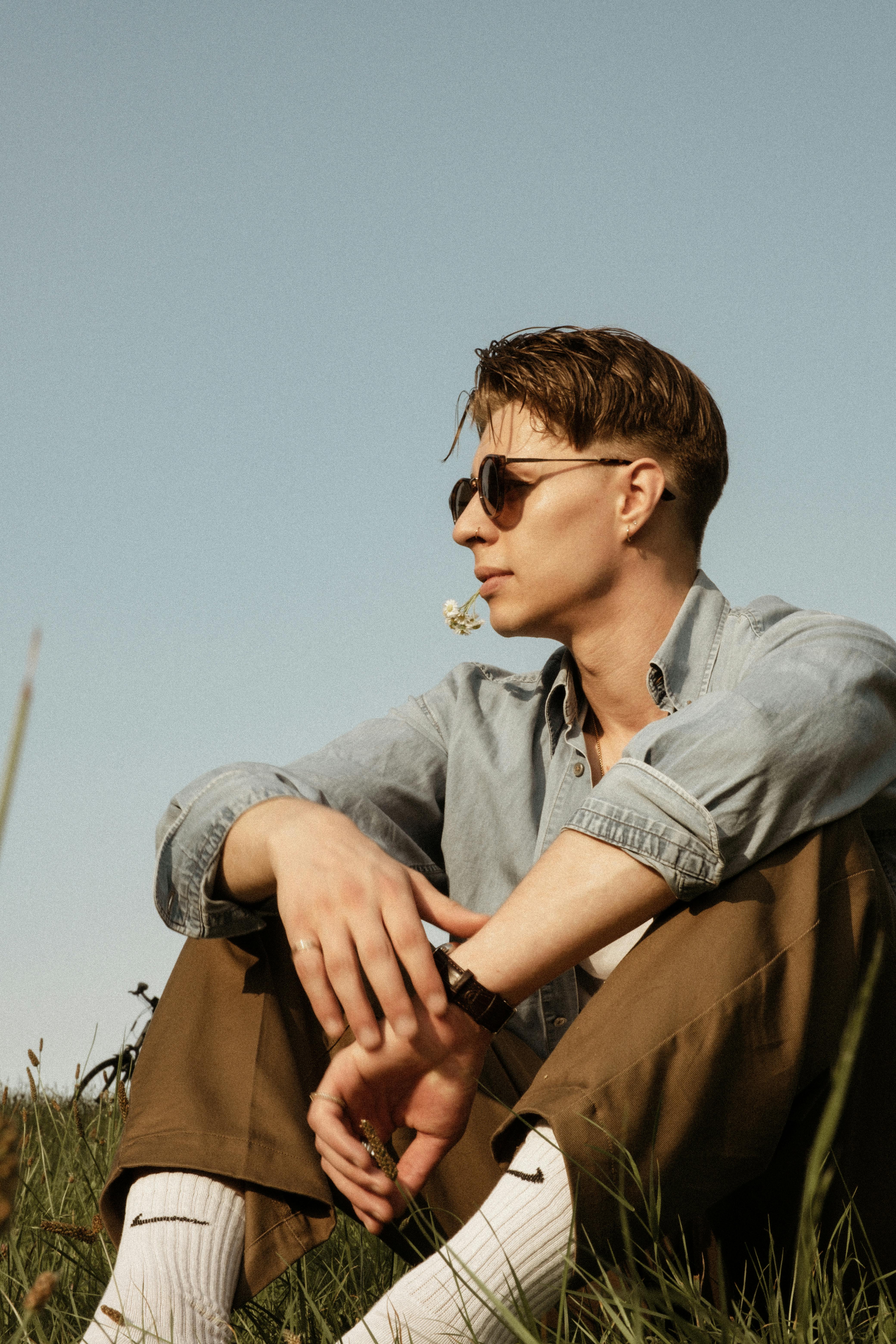 Stylish man sitting outdoors on a sunny day, enjoying nature and relaxation.