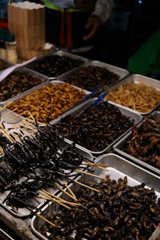 Various trays of edible insects including scorpions and beetles displayed at a market stall.
