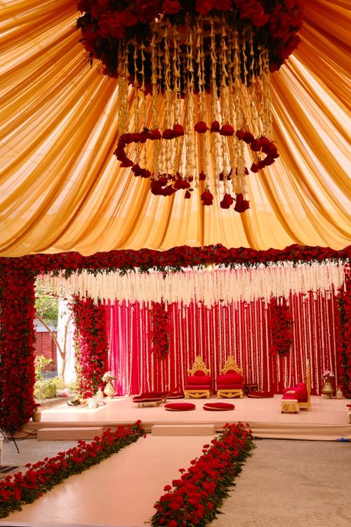 Free Elegant wedding ceremony setup with red roses, gold accents, and draped fabric in a luxurious setting. Stock Photo
