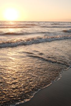 Peaceful ocean scene with waves gently lapping the sandy shore at sunset.