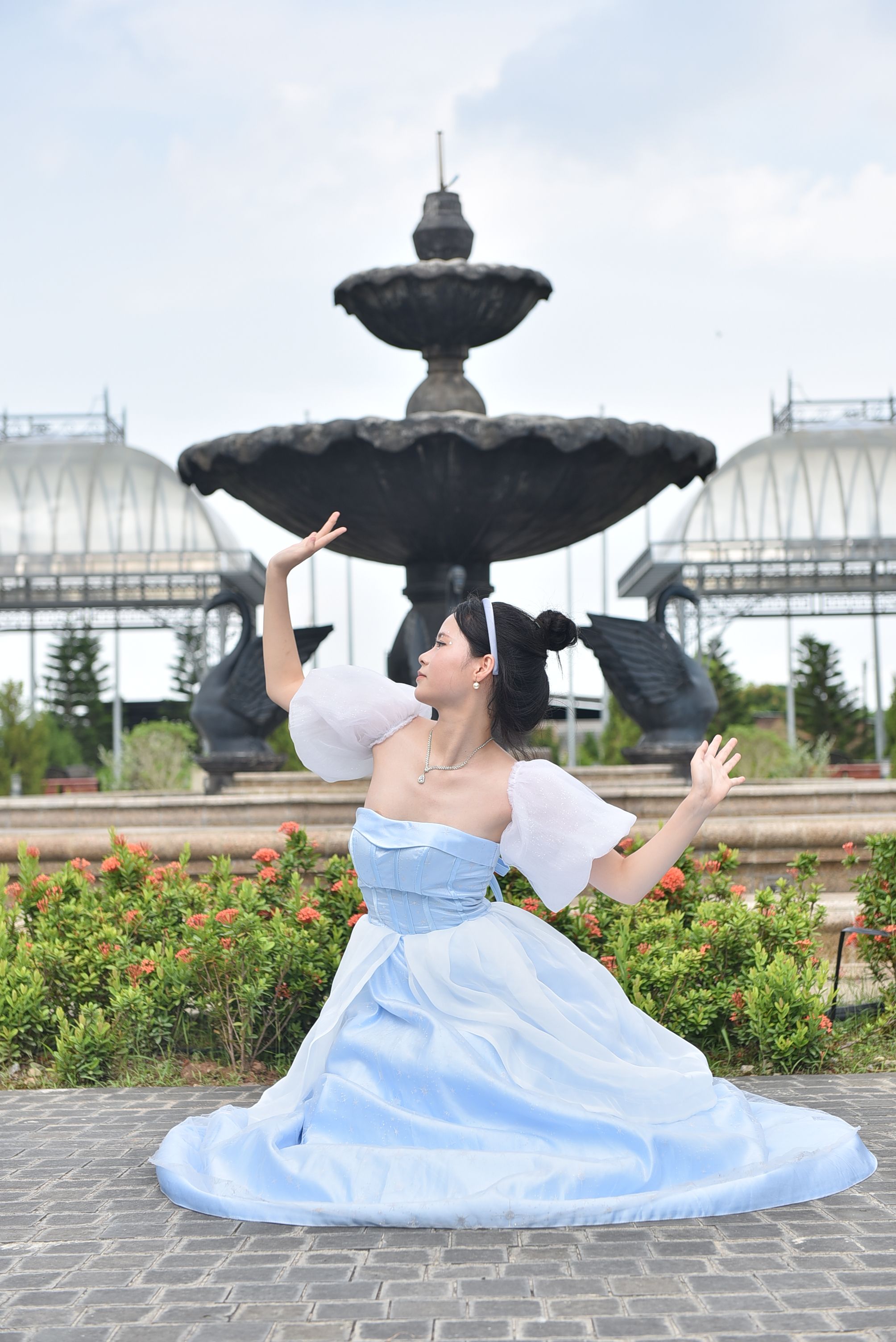 Woman in a flowing blue dress posing gracefully in front of a large fountain.