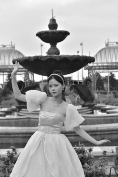 A bride stands elegantly before a fountain, showcasing her flowing dress in a monochrome setting.