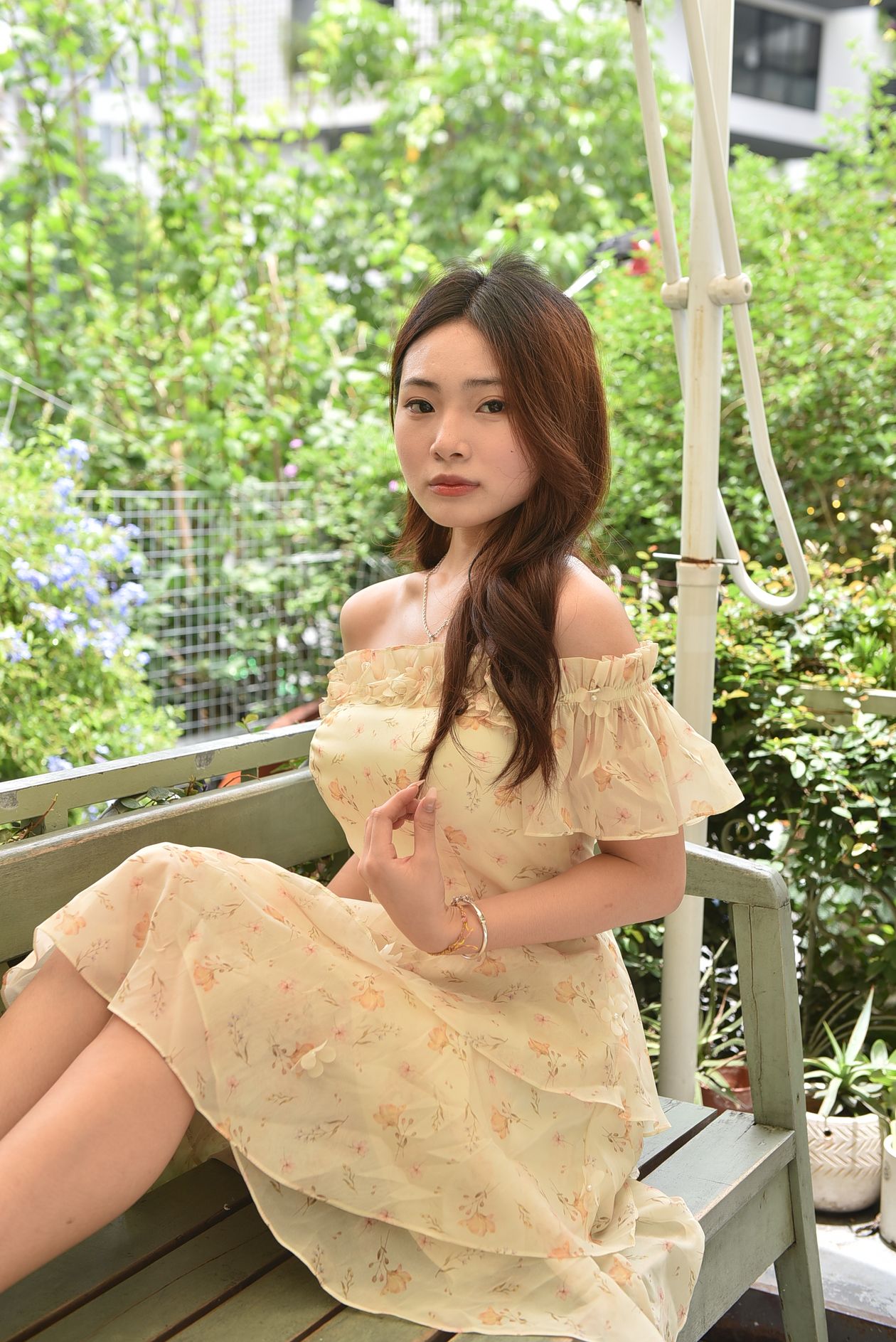Woman in a pale yellow floral midi dress sitting on a garden bench