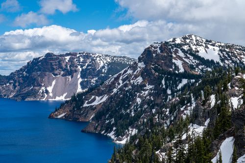 Free Stunning snow-capped mountains overlooking Crater Lake under a blue sky, capturing nature's beauty. Stock Photo
