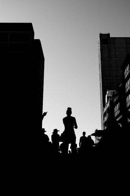 Dramatic black and white silhouette of people in an urban environment with towering buildings.