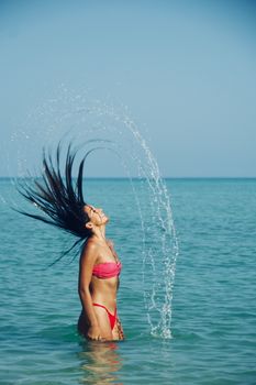 Woman in pink bikini enjoying a sunny day at the beach in Progreso, Mexico, with hair flipping water.