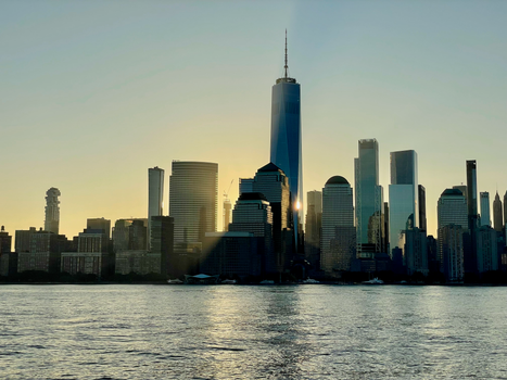 Sunset over New York's skyline, highlighting iconic skyscrapers and waterfront reflections.