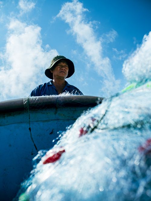 Free A fisherman works with nets on a boat in Lang Phuoc Hai, Vietnam against a bright blue sky. Stock Photo