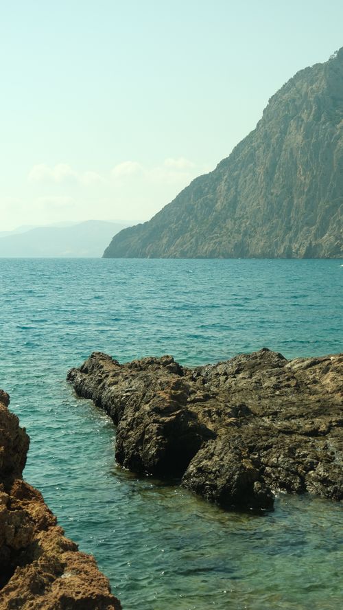 Free Explore the tranquil beauty of a rocky beach with clear blue waters and majestic cliffs in this serene coastal landscape image. Stock Photo