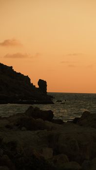 A tranquil coastal scene with a rocky cliff silhouette at sunset.